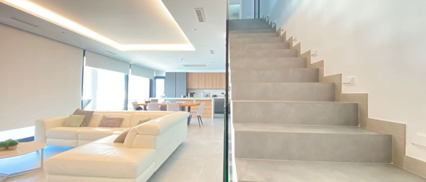 Escalera interior moderna de obra forrada con gres porcelánico gris de Gres Aragón, mostrando continuidad con el suelo del salón.